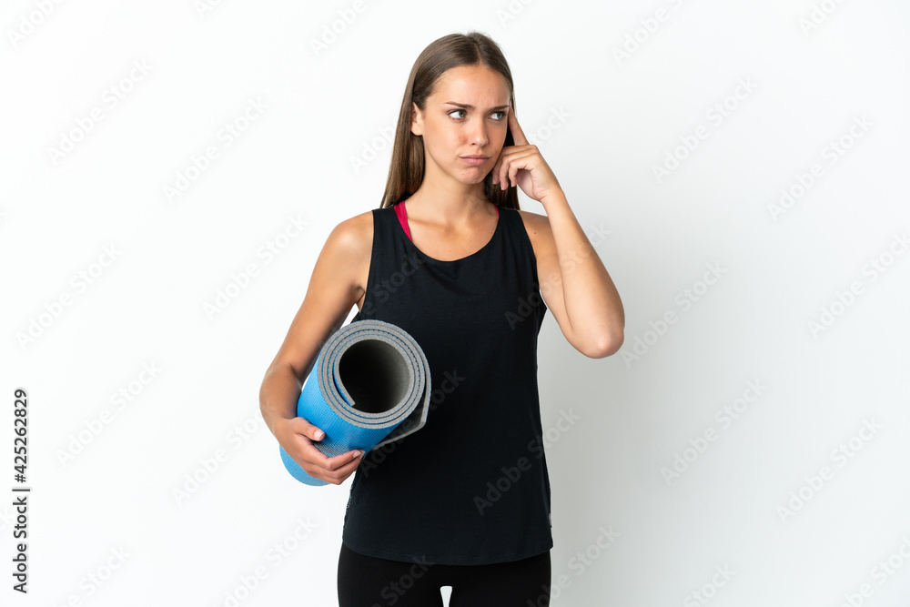 Sport woman going to yoga classes while holding a mat over isolated white background having doubts and thinking Sport woman going to yoga classes while holding a mat over isolated white background having doubts and thinking