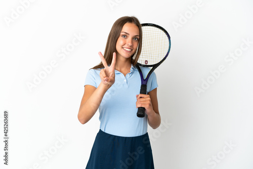 Woman playing tennis over isolated white wall smiling and showing victory sign © luismolinero