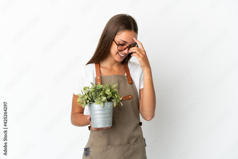 Gardener girl holding a plant over isolated white background laughing Gardener girl holding a plant over isolated white background laughing