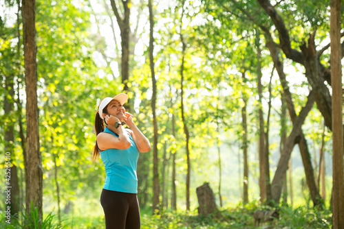 Healthy athletic woman listening to music before go running to be more relaxed in the nature park. Asian runner woman relaxed. Heathy and Lifestyle concept. On Nature background.