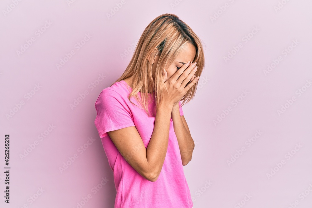 Beautiful blonde woman wearing casual pink tshirt with sad expression covering face with hands while crying. depression concept. Beautiful blonde woman wearing casual pink tshirt with sad expression covering face with hands while crying. depression concept.