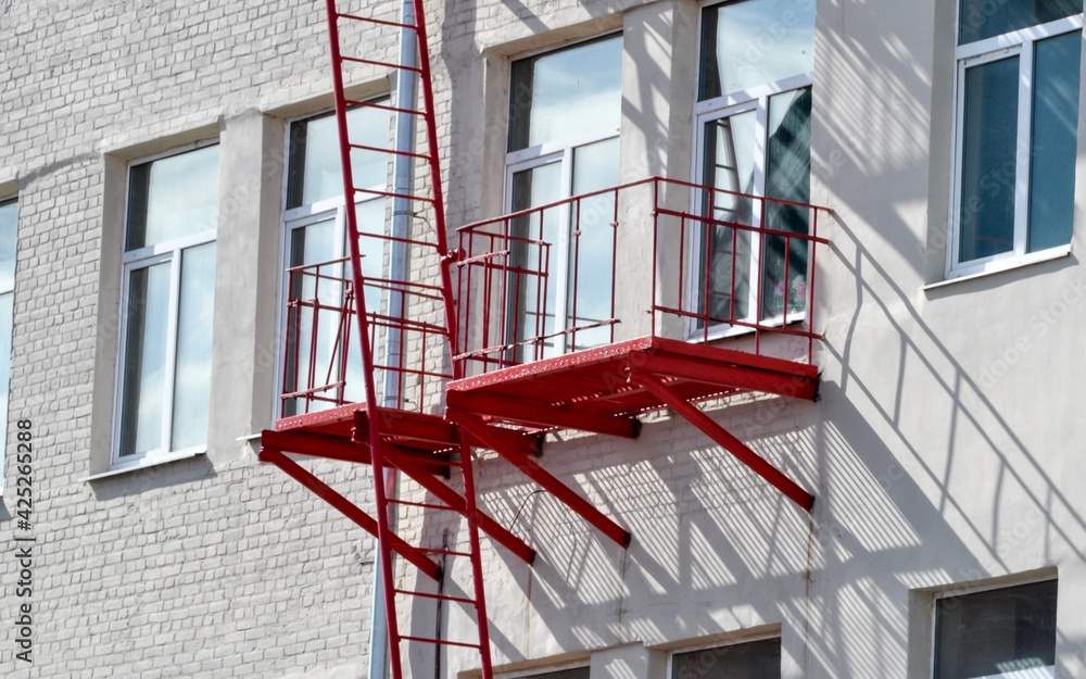 architectural details - red balcony escape stairs in case of fire. Accents of architecture. The steel structure is red in color. urban environment. windows and balcony of the building. architectural details - red balcony escape stairs in case of fire. Accents of architecture. The steel structure is red in color. urban environment. windows and balcony of the building.