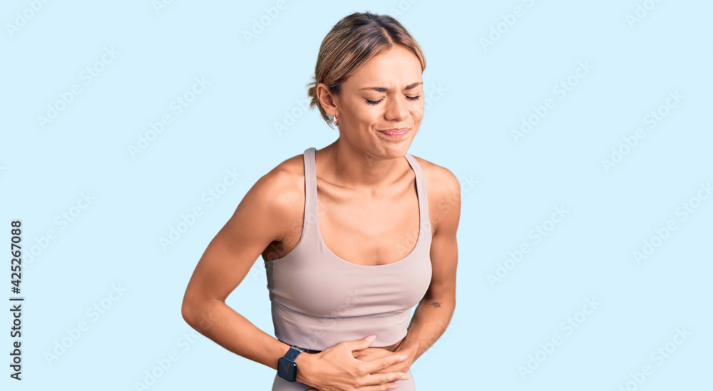 Beautiful caucasian woman wearing sportswear with hand on stomach because indigestion, painful illness feeling unwell. ache concept. Beautiful caucasian woman wearing sportswear with hand on stomach because indigestion, painful illness feeling unwell. ache concept.
