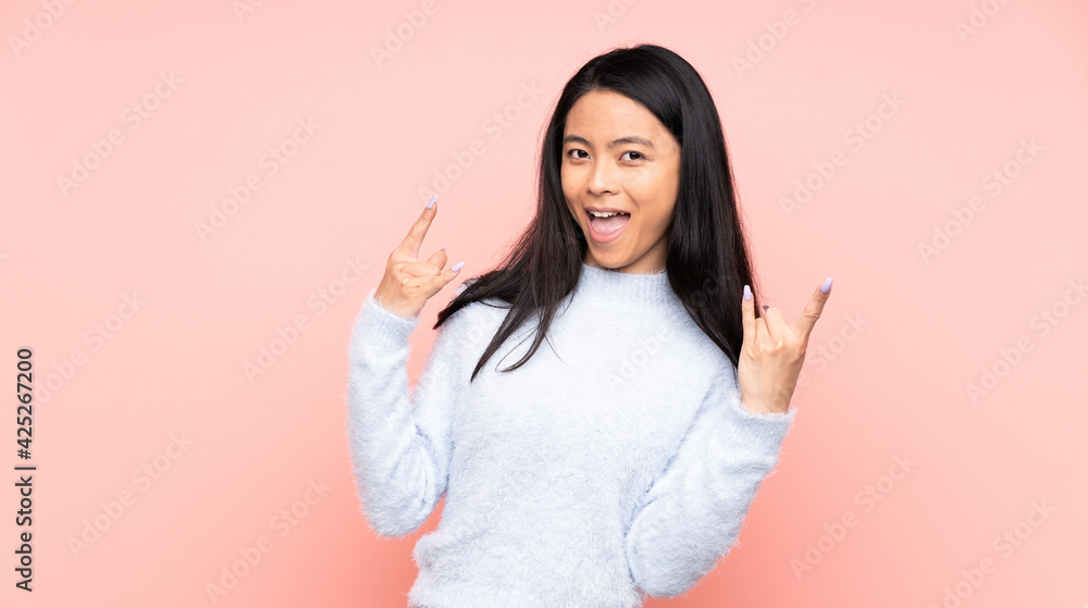 Teenager Chinese woman isolated on pink background making horn gesture Teenager Chinese woman isolated on pink background making horn gesture