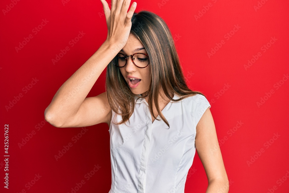 Young brunette woman wearing casual clothes and glasses surprised with hand on head for mistake, remember error. forgot, bad memory concept. Young brunette woman wearing casual clothes and glasses surprised with hand on head for mistake, remember error. forgot, bad memory concept.