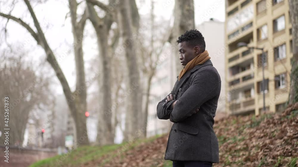 Black man arms crossed standing outside at park thinking wearing winter coat and scarf Black man arms crossed standing outside at park thinking wearing winter coat and scarf