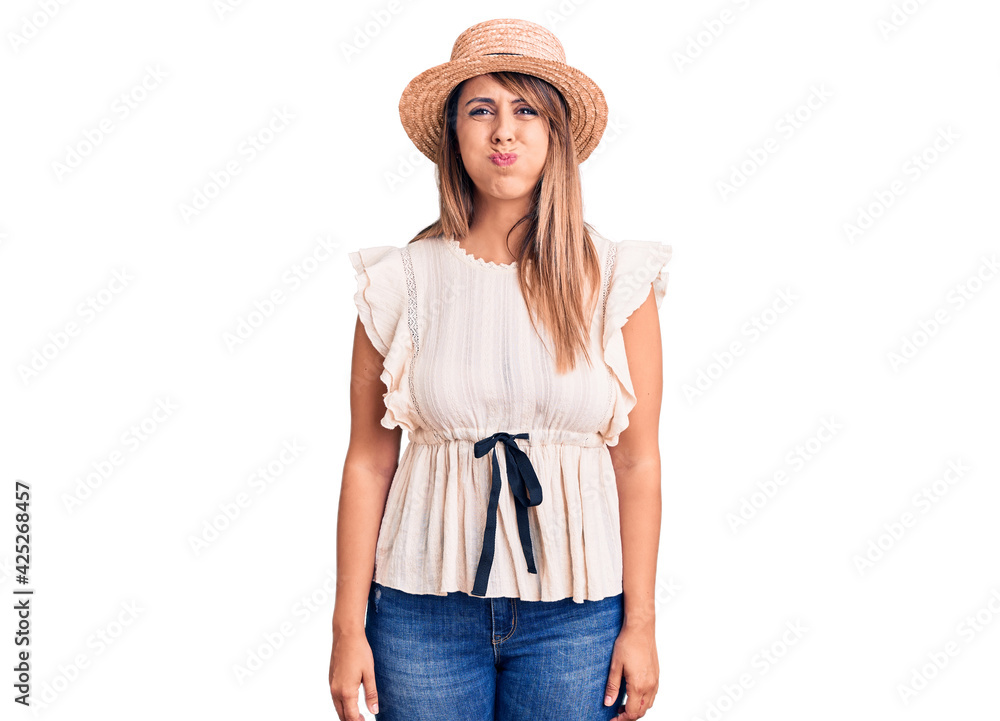 Young beautiful woman wearing summer hat and t-shirt puffing cheeks with funny face. mouth inflated with air, crazy expression. Young beautiful woman wearing summer hat and t-shirt puffing cheeks with funny face. mouth inflated with air, crazy expression.