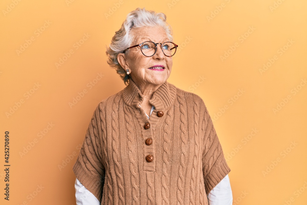 Senior grey-haired woman wearing casual clothes and glasses smiling looking to the side and staring away thinking. Senior grey-haired woman wearing casual clothes and glasses smiling looking to the side and staring away thinking.