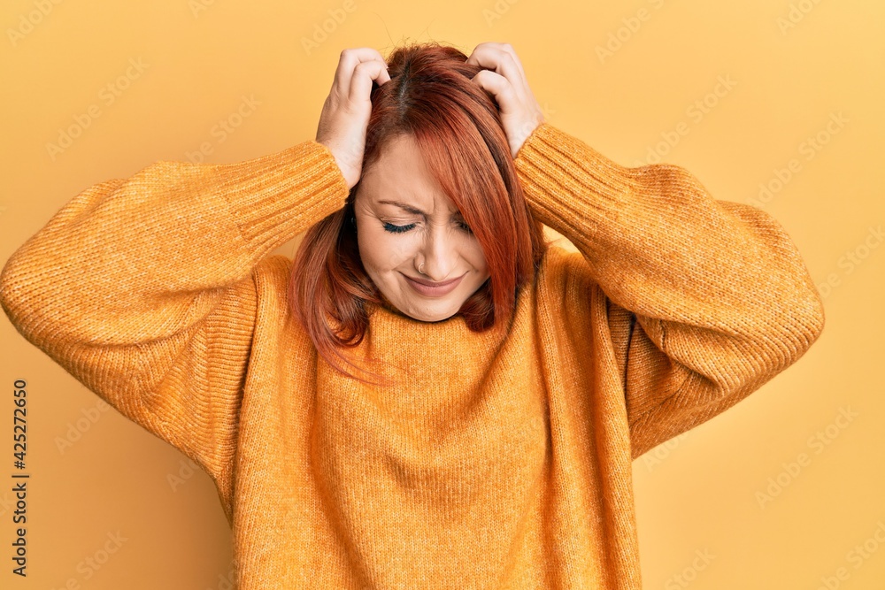 Beautiful redhead woman wearing casual winter sweater over yellow background suffering from headache desperate and stressed because pain and migraine. hands on head. Beautiful redhead woman wearing casual winter sweater over yellow background suffering from headache desperate and stressed because pain and migraine. hands on head.