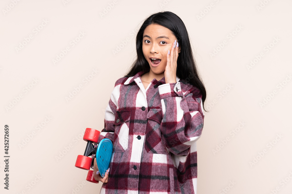 Teenager Chinese girl isolated on beige background with a skate and doing surprise gesture Teenager Chinese girl isolated on beige background with a skate and doing surprise gesture