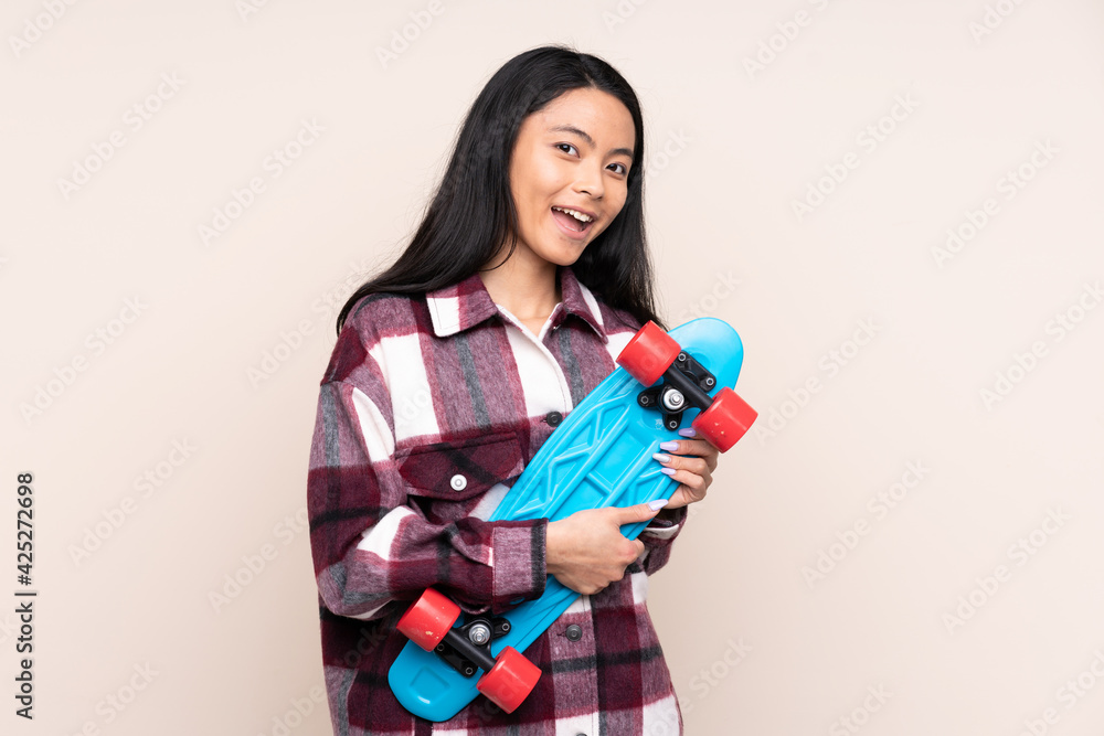 Teenager Chinese girl isolated on beige background with a skate with happy expression Teenager Chinese girl isolated on beige background with a skate with happy expression