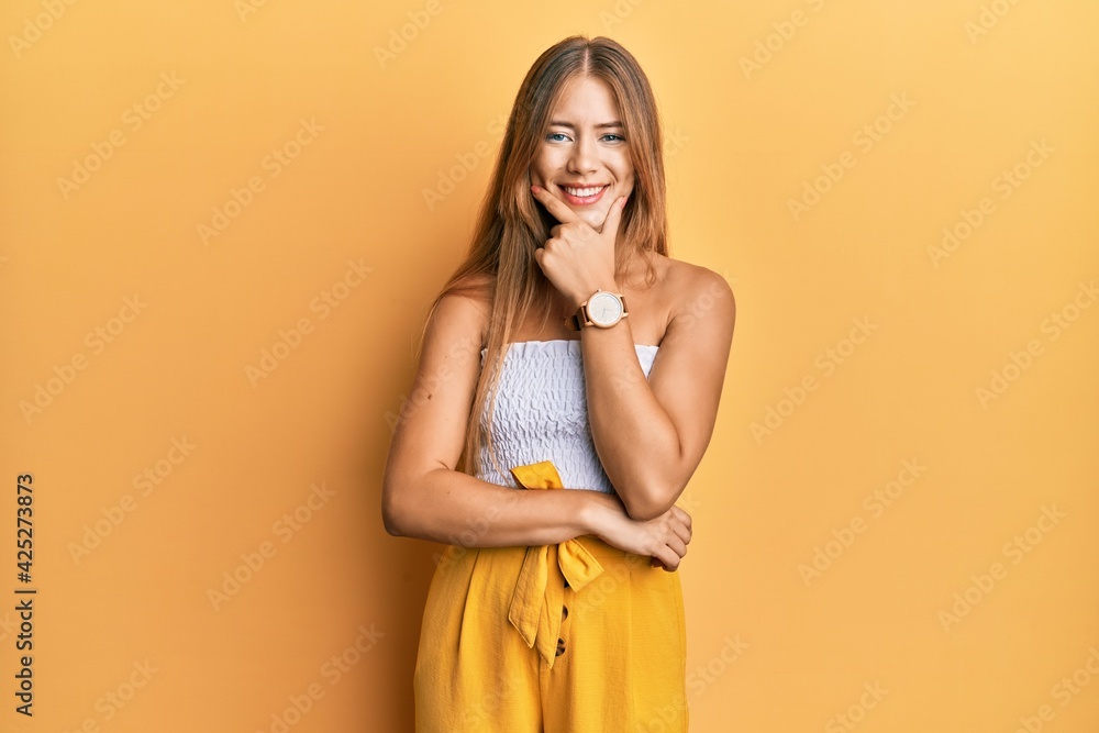 Beautiful young blonde woman wearing casual summer clothes looking confident at the camera smiling with crossed arms and hand raised on chin. thinking positive. Beautiful young blonde woman wearing casual summer clothes looking confident at the camera smiling with crossed arms and hand raised on chin. thinking positive.