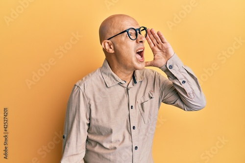 Middle age bald man wearing casual clothes and glasses shouting and screaming loud to side with hand on mouth. communication concept. © Krakenimages.com