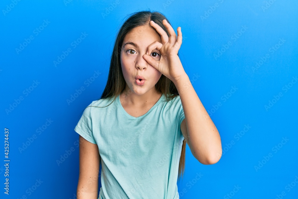 Beautiful brunette little girl wearing casual white t shirt doing ok gesture shocked with surprised face, eye looking through fingers. unbelieving expression. Beautiful brunette little girl wearing casual white t shirt doing ok gesture shocked with surprised face, eye looking through fingers. unbelieving expression.
