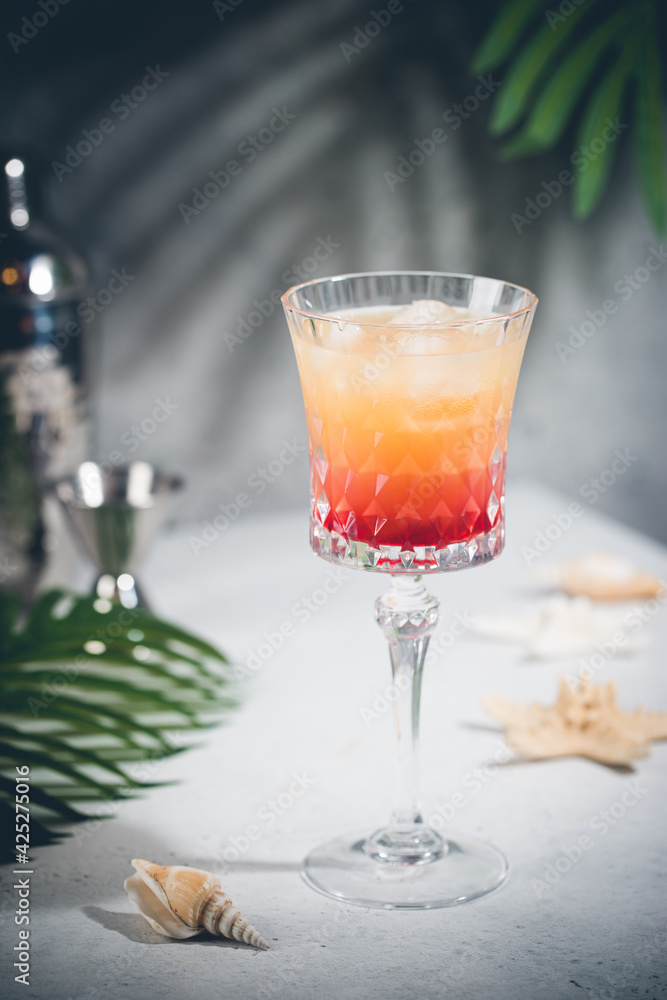 Colourful exotic Tequila Sunrise cocktail in a glass served with ice on gray background Colourful exotic Tequila Sunrise cocktail in a glass served with ice on gray background