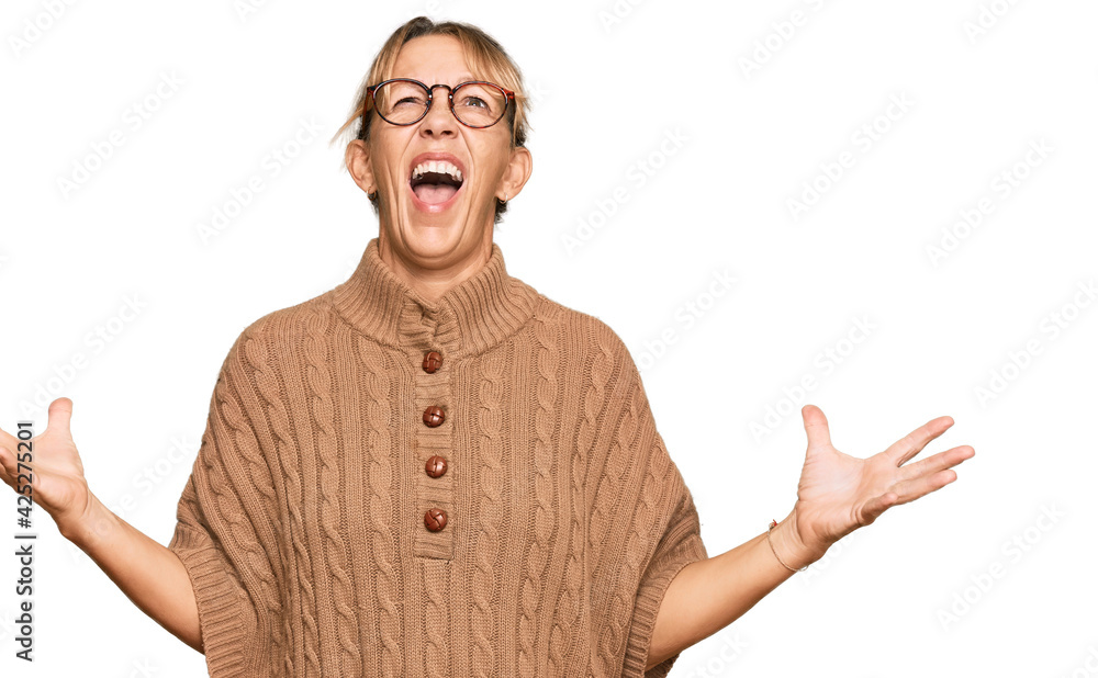 Middle age blonde woman wearing sweater and glasses crazy and mad shouting and yelling with aggressive expression and arms raised. frustration concept. Middle age blonde woman wearing sweater and glasses crazy and mad shouting and yelling with aggressive expression and arms raised. frustration concept.