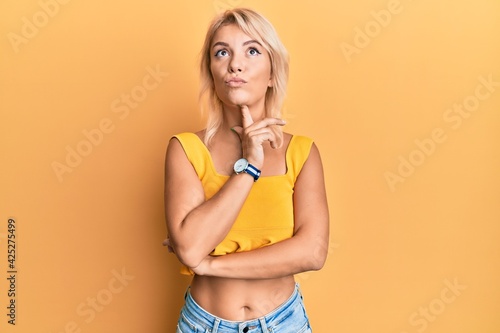 Young blonde girl wearing casual clothes thinking concentrated about doubt with finger on chin and looking up wondering