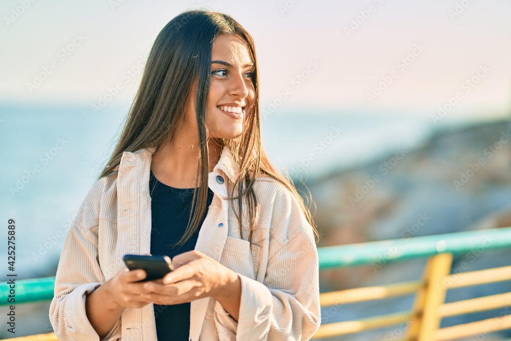 Young hispanic girl smiling happy using smartphone at the promenade. Young hispanic girl smiling happy using smartphone at the promenade.