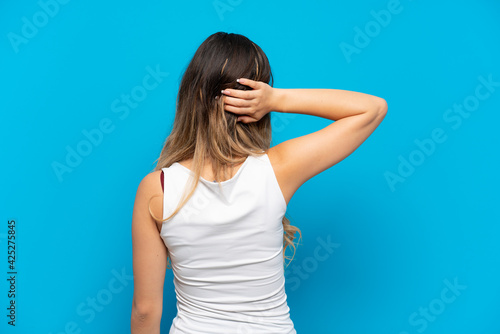 Young Russian girl isolated on blue background in back position and thinking