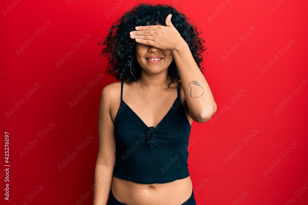 Young hispanic woman wearing casual style with sleeveless shirt smiling and laughing with hand on face covering eyes for surprise. blind concept. Young hispanic woman wearing casual style with sleeveless shirt smiling and laughing with hand on face covering eyes for surprise. blind concept.