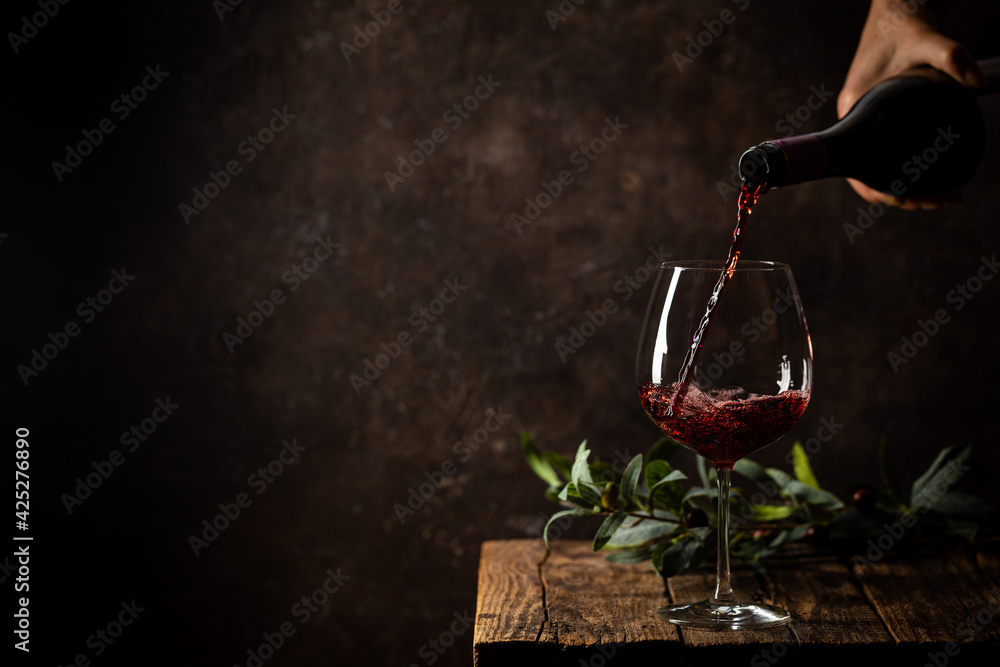 Pouring red wine into the glass against rustic dark wooden background - obrazy, fototapety, plakaty 