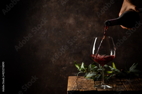 Slika na platnu Pouring red wine into the glass against rustic dark wooden background