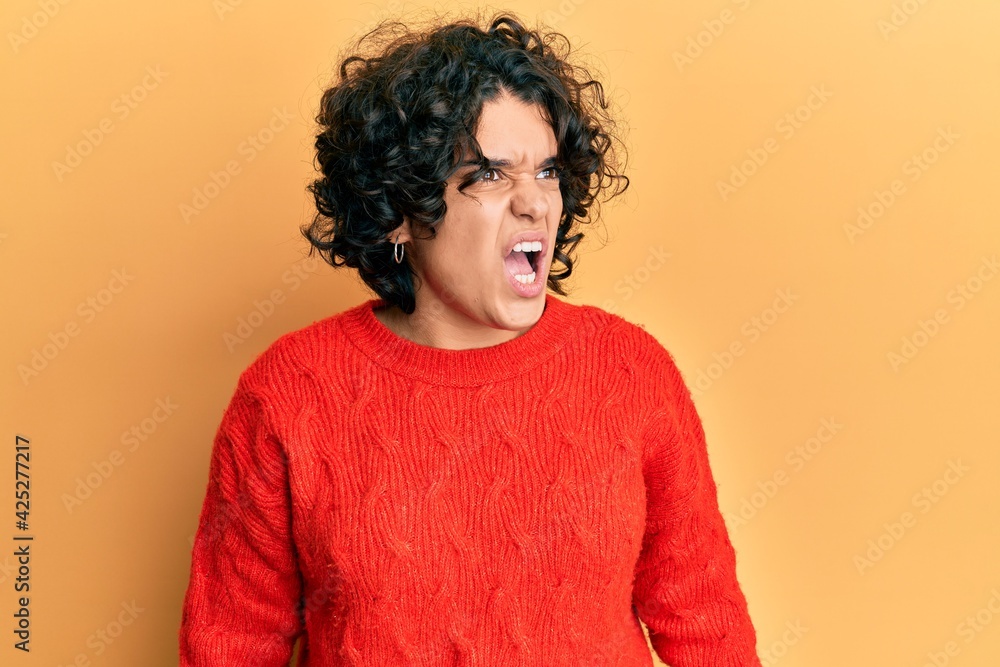Young hispanic woman with curly hair wearing casual winter sweater angry and mad screaming frustrated and furious, shouting with anger. rage and aggressive concept. Young hispanic woman with curly hair wearing casual winter sweater angry and mad screaming frustrated and furious, shouting with anger. rage and aggressive concept.