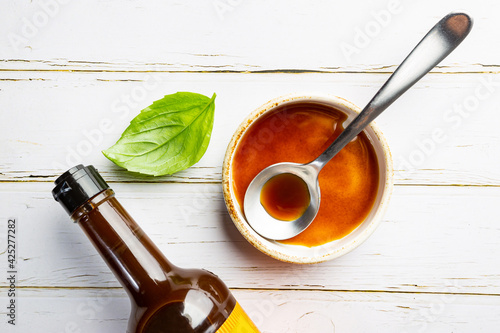 Worcestershire sauce in a bowl with spoon and bottle over white background, top view photo