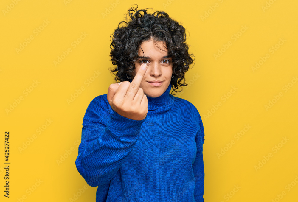 Young hispanic woman with curly hair wearing turtleneck sweater showing middle finger, impolite and rude fuck off expression Young hispanic woman with curly hair wearing turtleneck sweater showing middle finger, impolite and rude fuck off expression