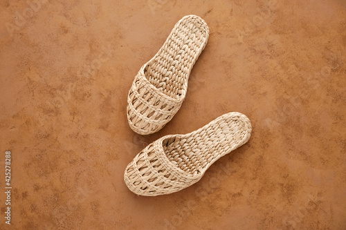 Comfortable and stylish home or beach slippers made of natural tropical rattan. Brown background. View from above. Safe for the environment. Zero waste and sustainable free lifestyle. 