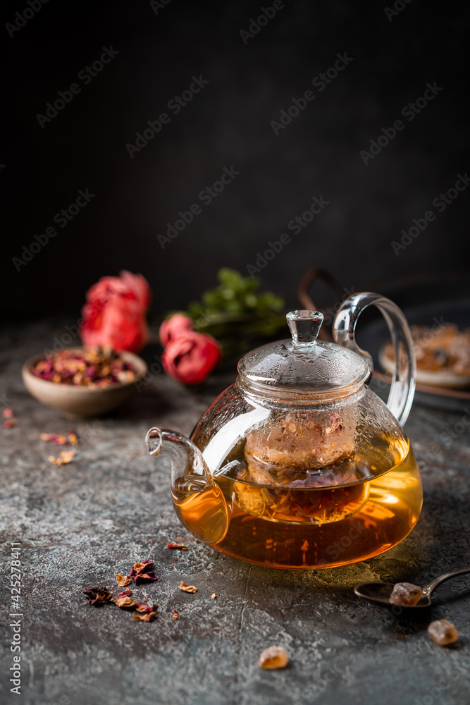 herbal flower tea from the petals of rose in a glass teapot on dark gray background