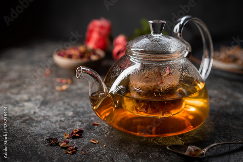 herbal flower tea from the petals of rose in a glass teapot on dark gray background