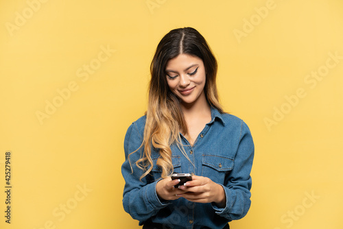 Young Russian girl isolated on yellow background sending a message with the mobile