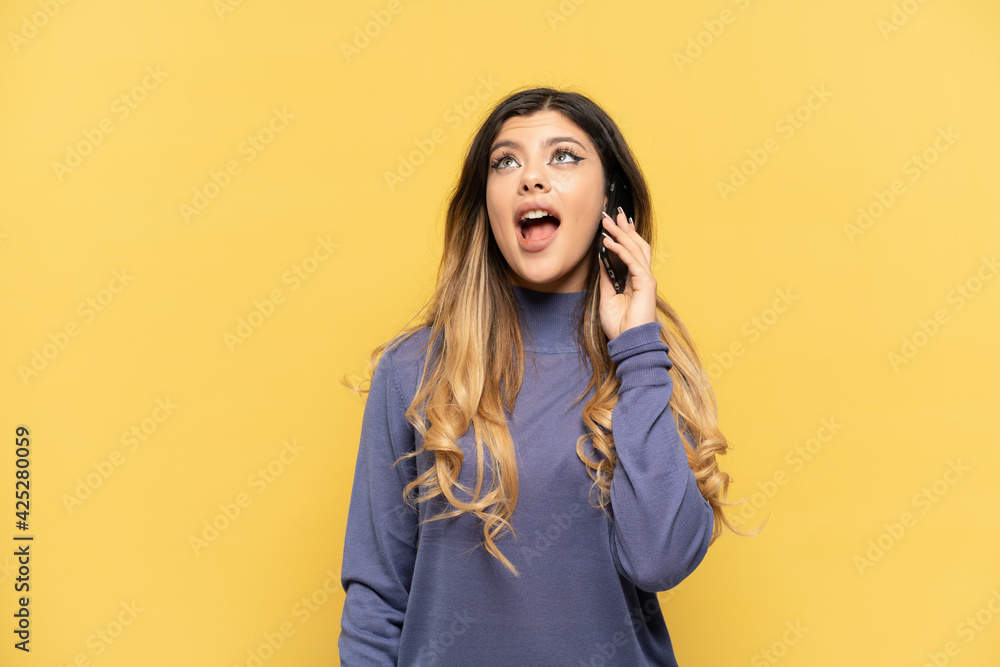 Young Russian girl using mobile phone isolated on yellow background laughing Young Russian girl using mobile phone isolated on yellow background laughing