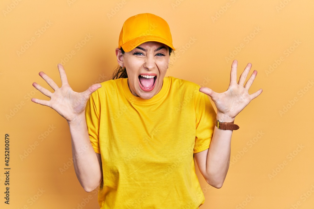 Young hispanic woman wearing delivery uniform and cap celebrating crazy and amazed for success with arms raised and open eyes screaming excited. winner concept