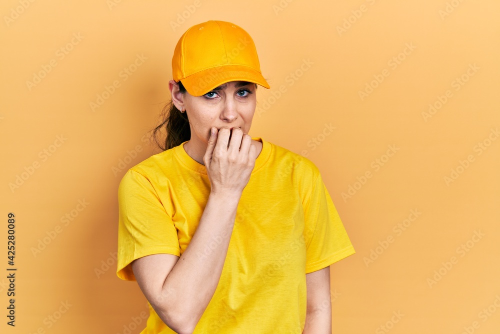Young hispanic woman wearing delivery uniform and cap looking stressed and nervous with hands on mouth biting nails. anxiety problem.