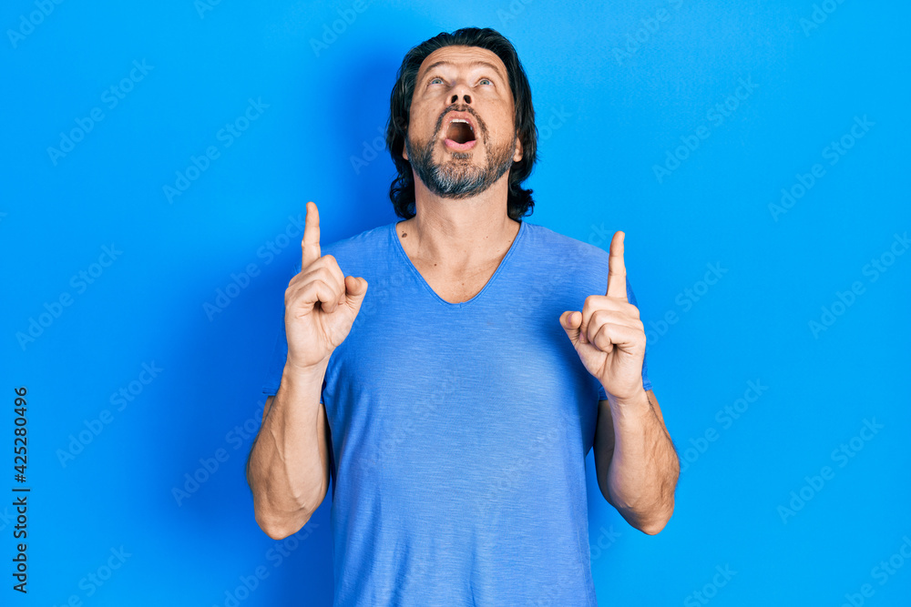Middle age caucasian man wearing casual clothes amazed and surprised looking up and pointing with fingers and raised arms. Middle age caucasian man wearing casual clothes amazed and surprised looking up and pointing with fingers and raised arms.