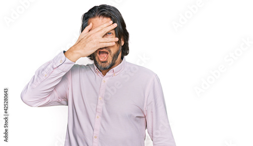 Middle age handsome man wearing business shirt peeking in shock covering face and eyes with hand, looking through fingers with embarrassed expression.