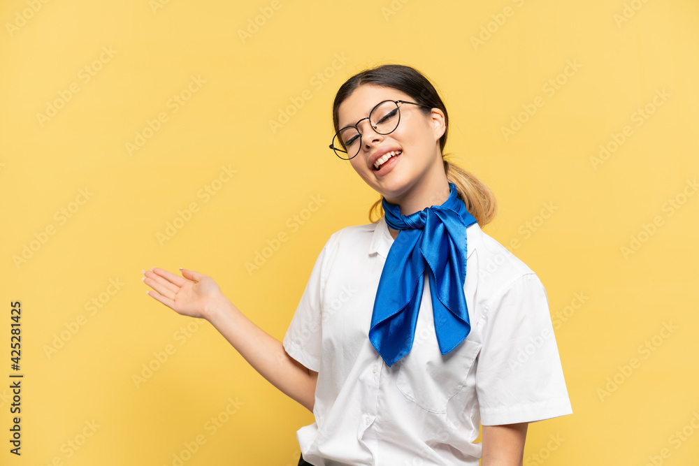 Airplane stewardess isolated on yellow background extending hands to the side for inviting to come Airplane stewardess isolated on yellow background extending hands to the side for inviting to come