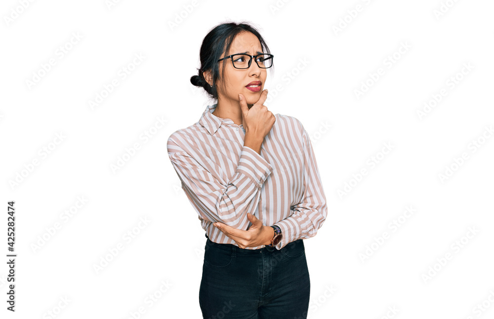 Young hispanic girl wearing casual clothes and glasses thinking worried about a question, concerned and nervous with hand on chin Young hispanic girl wearing casual clothes and glasses thinking worried about a question, concerned and nervous with hand on chin
