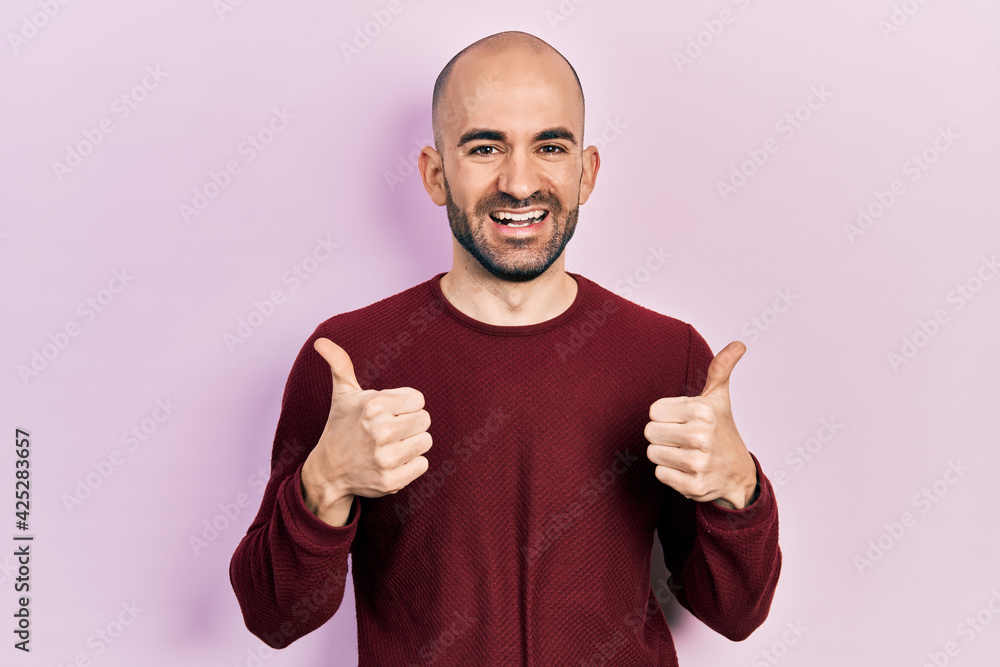 Young bald man wearing casual clothes success sign doing positive gesture with hand, thumbs up smiling and happy. cheerful expression and winner gesture. Young bald man wearing casual clothes success sign doing positive gesture with hand, thumbs up smiling and happy. cheerful expression and winner gesture.