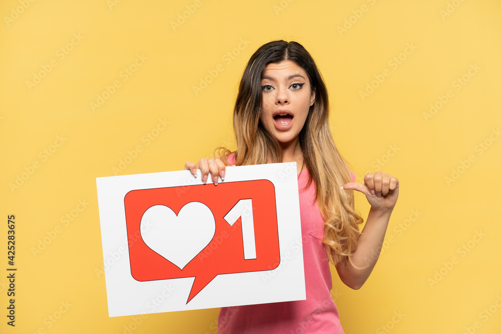 Young Russian girl isolated on yellow background holding a placard with Like icon and pointing it Young Russian girl isolated on yellow background holding a placard with Like icon and pointing it