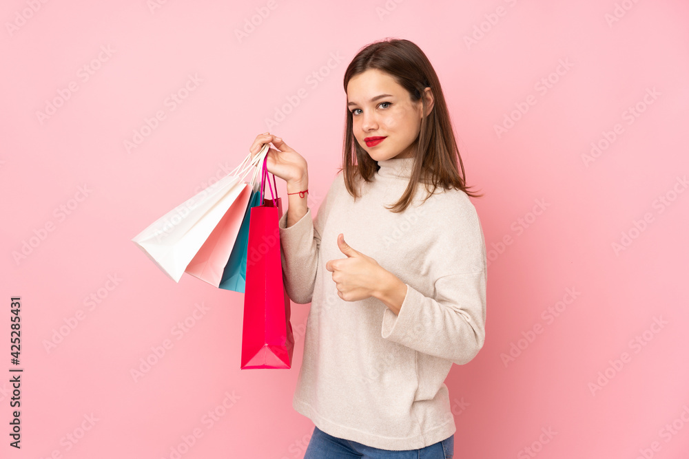Teenager girl isolated on pink background holding shopping bags and with thumb up