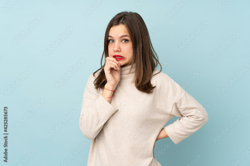 Teenager girl isolated on blue background nervous and scared