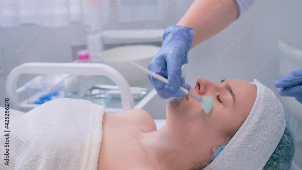 Cosmetologist applying face moisturizing mask on young woman's face Cosmetologist applying face moisturizing mask on young woman's face