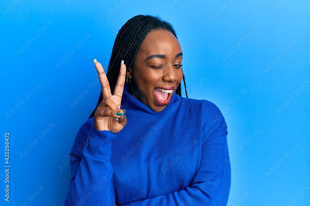Young african american woman wearing casual winter sweater smiling with happy face winking at the camera doing victory sign. number two. Young african american woman wearing casual winter sweater smiling with happy face winking at the camera doing victory sign. number two.
