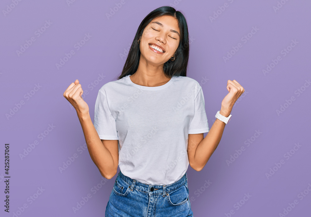 Beautiful young asian woman wearing casual white t shirt very happy and excited doing winner gesture with arms raised, smiling and screaming for success. celebration concept. Beautiful young asian woman wearing casual white t shirt very happy and excited doing winner gesture with arms raised, smiling and screaming for success. celebration concept.