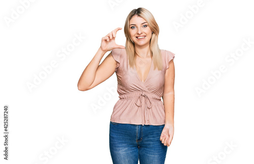 Young caucasian woman wearing casual clothes smiling and confident gesturing with hand doing small size sign with fingers looking and the camera. measure concept.
