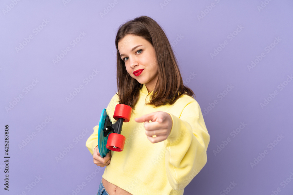 Teenager girl isolated on purple background with a skate and pointing to the front Teenager girl isolated on purple background with a skate and pointing to the front