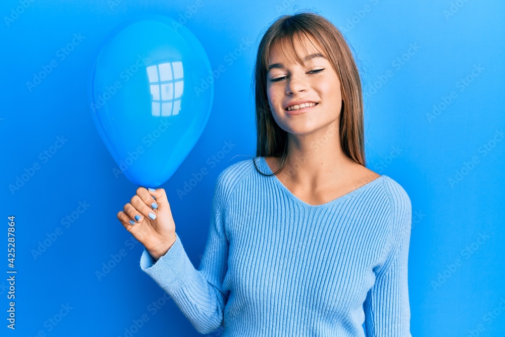 Caucasian woman holding a balloon over blue background Caucasian woman holding a balloon over blue background